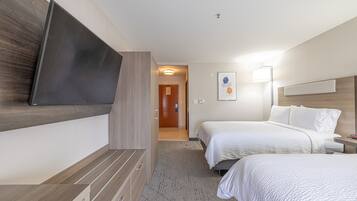 A hotel room with two beds, a flat-screen TV mounted on the wall, a bedside table, and a lamp.
