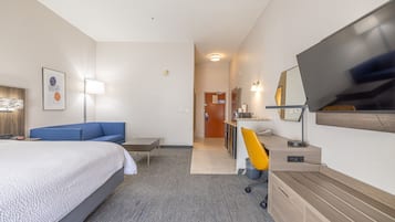 Habitación de hotel con cama, escritorio, silla, televisión y baño a la vista.