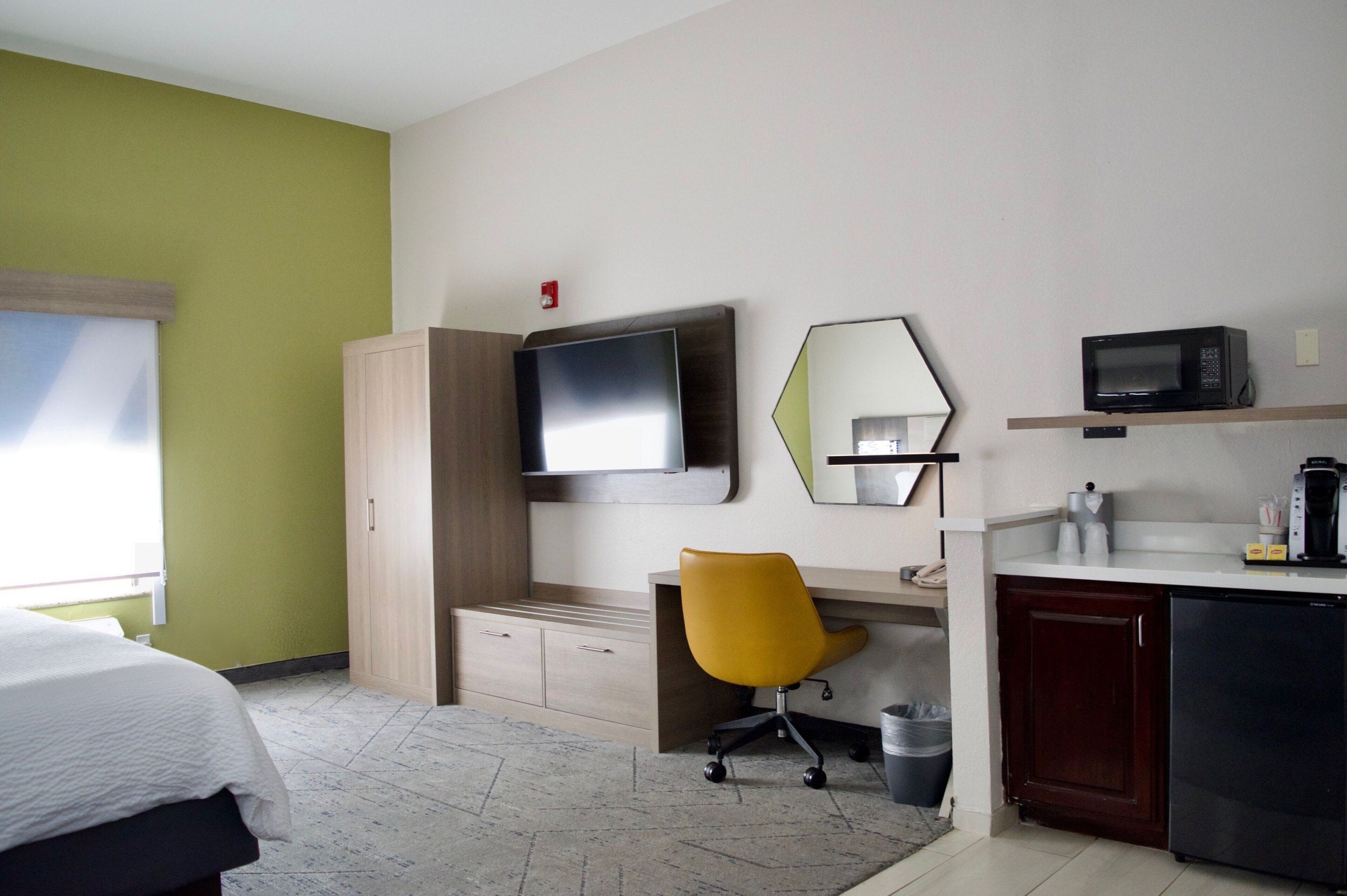 A hotel room with a bed, a desk with a chair, a television, a microwave, and a small kitchenette.