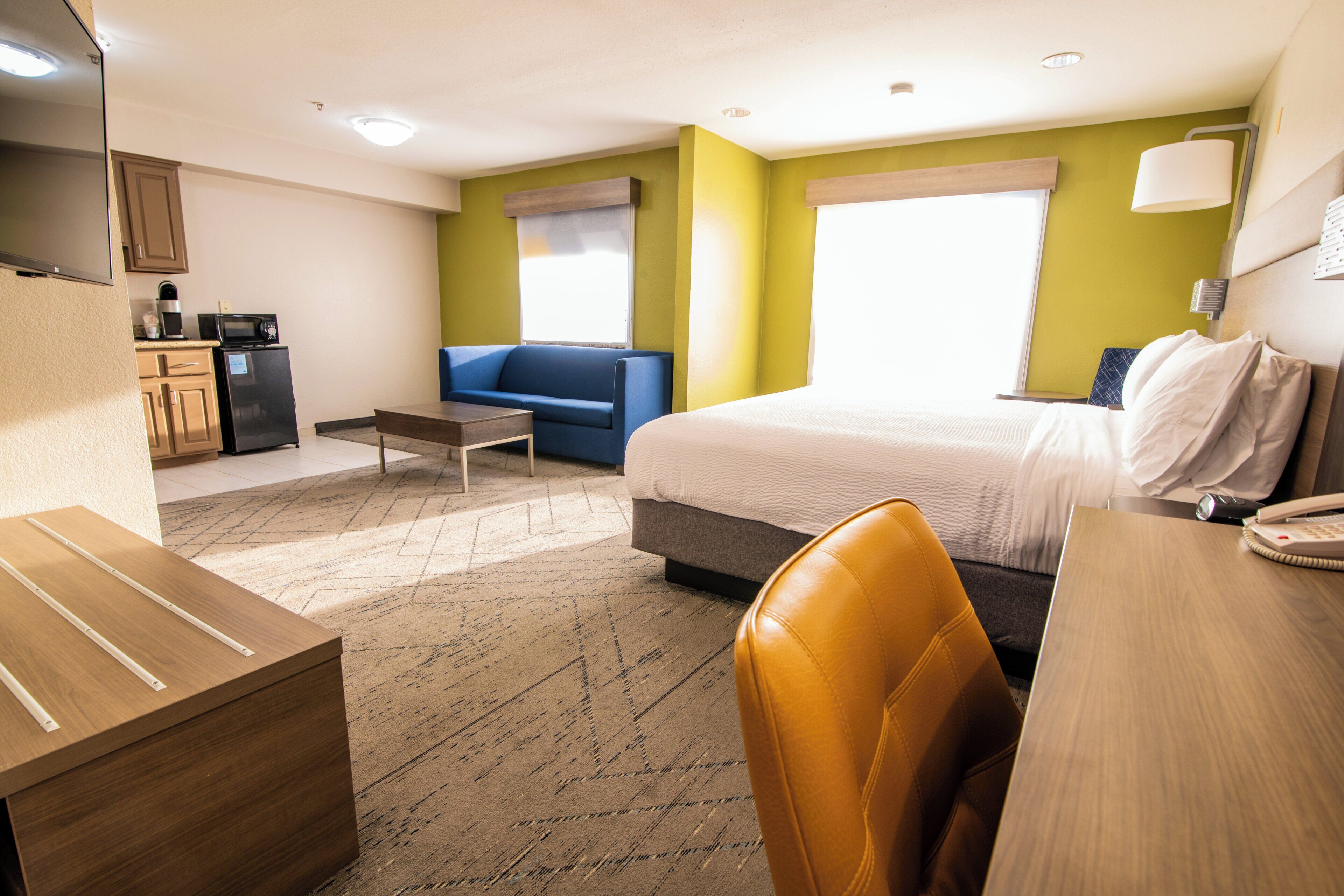 A hotel room with a bed, a desk, a chair, a sofa, a kitchenette, and a window.