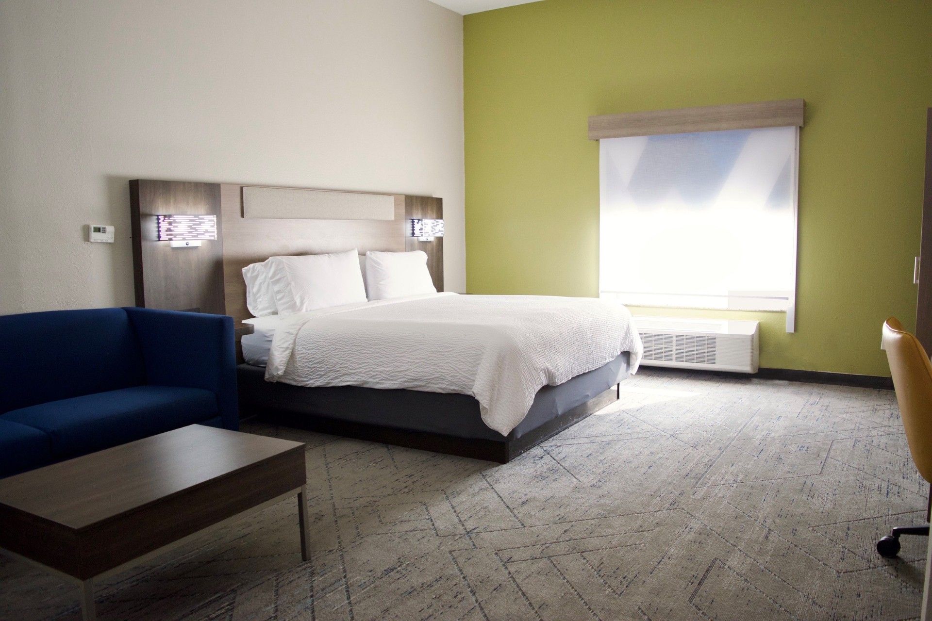 Una habitación de hotel con una cama, un sofá azul, una mesa de madera y una ventana con persianas.