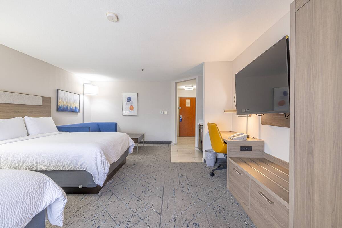 A hotel room with a bed, bedside table, chair, desk, TV, and artwork on the walls.