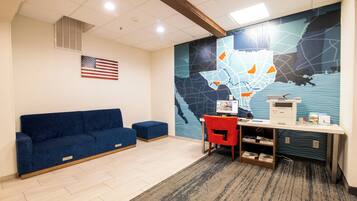 Una habitación con un sofá azul, una silla roja, un escritorio con una computadora y un mapa de pared.