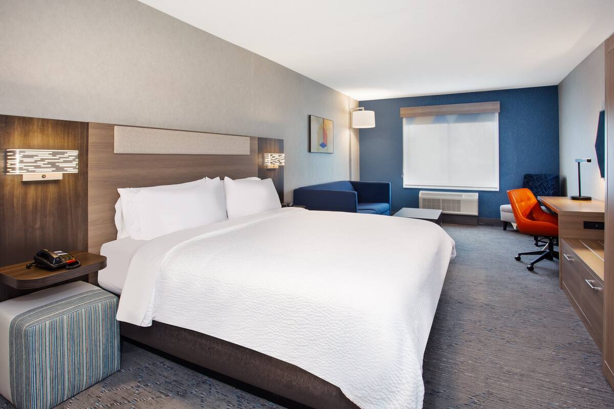 A hotel room with a large bed, a desk, an orange chair, and a small table.