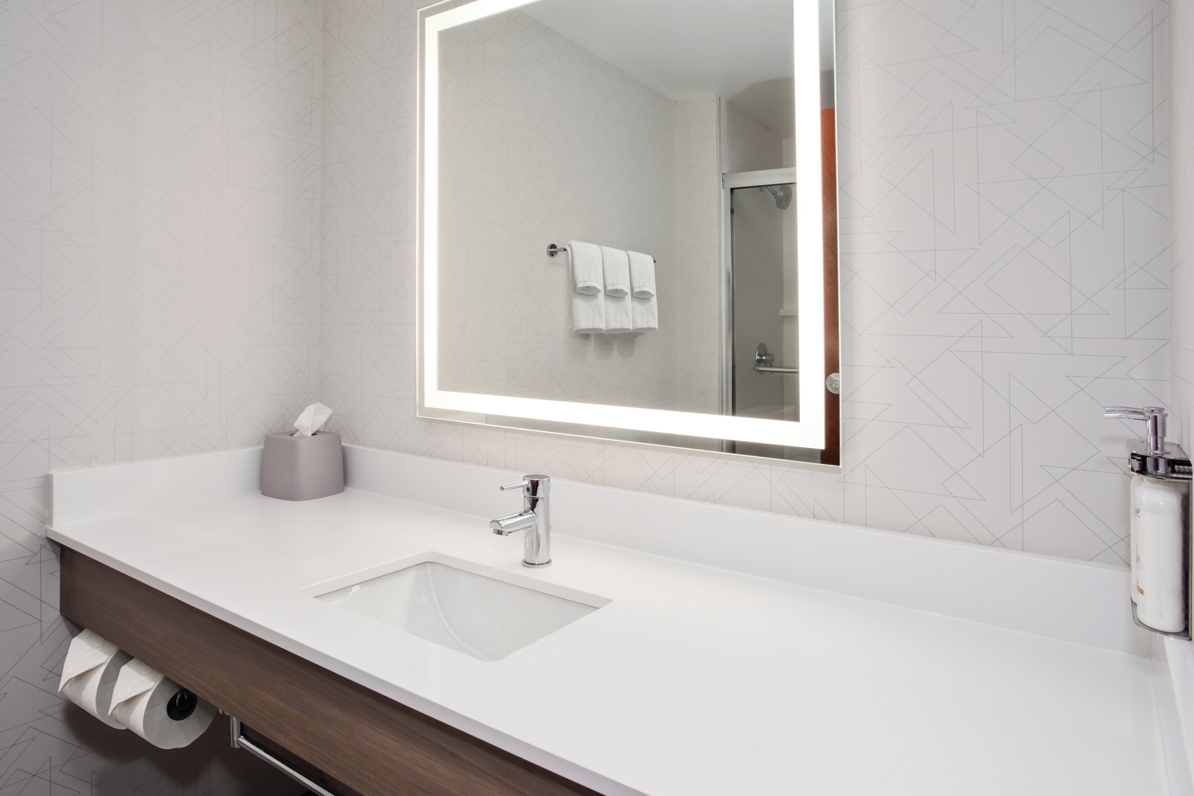 Un baño moderno con un lavamanos blanco, un espejo y un perchero para toallas.