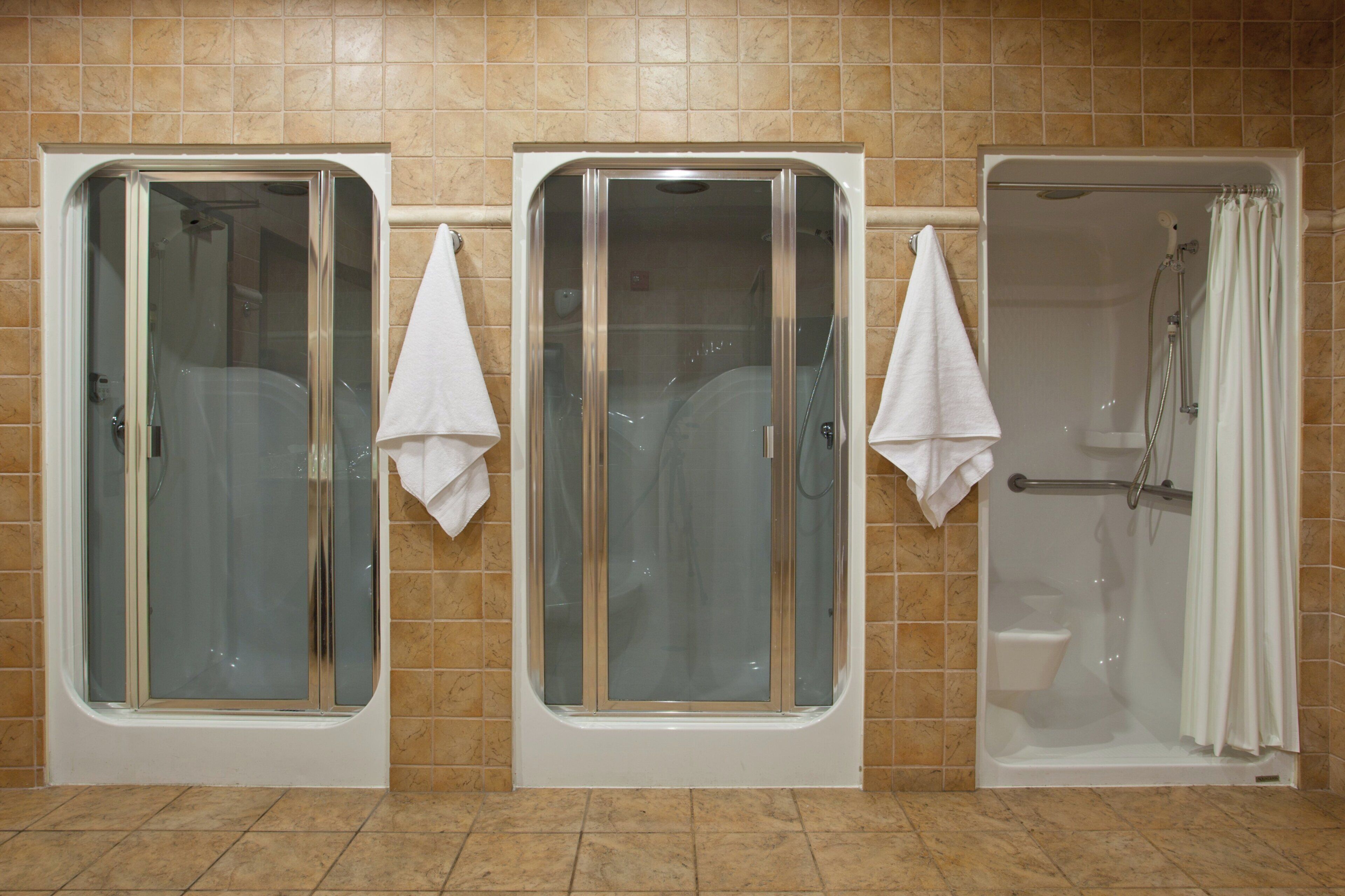 Une salle de bain avec trois cabines de douche en verre, chacune ayant une serviette blanche accrochée à la porte.