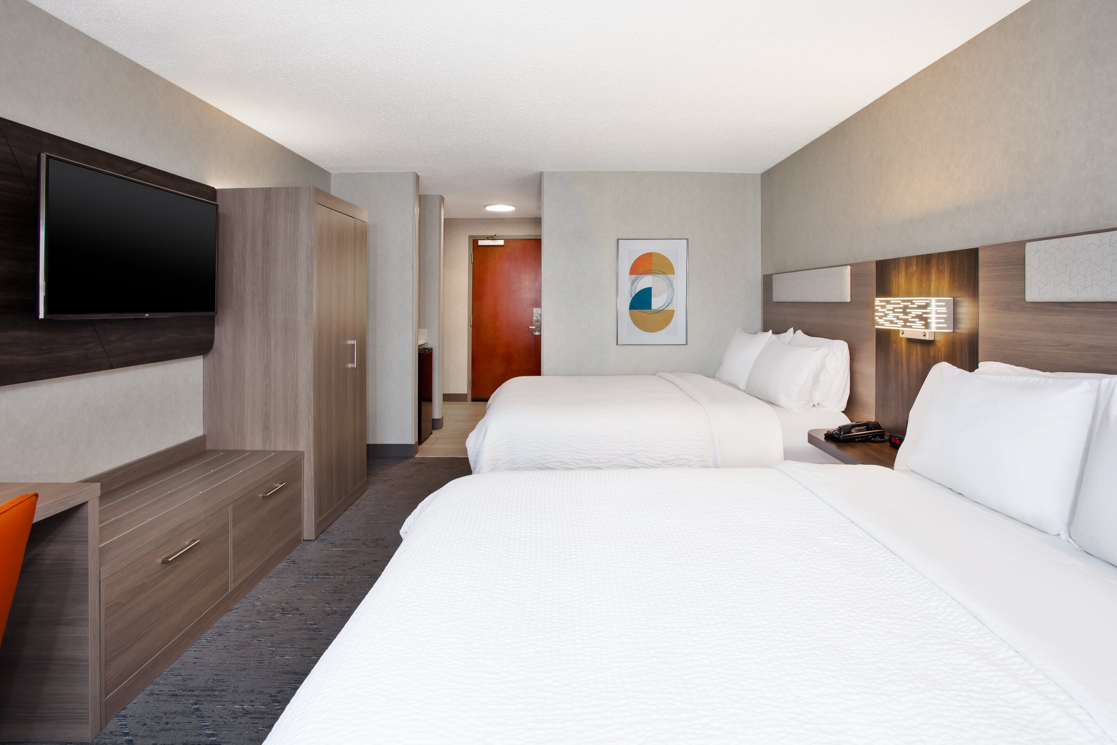 Een hotelkamer met twee bedden, een televisie, een bureau en een schilderij aan de muur.