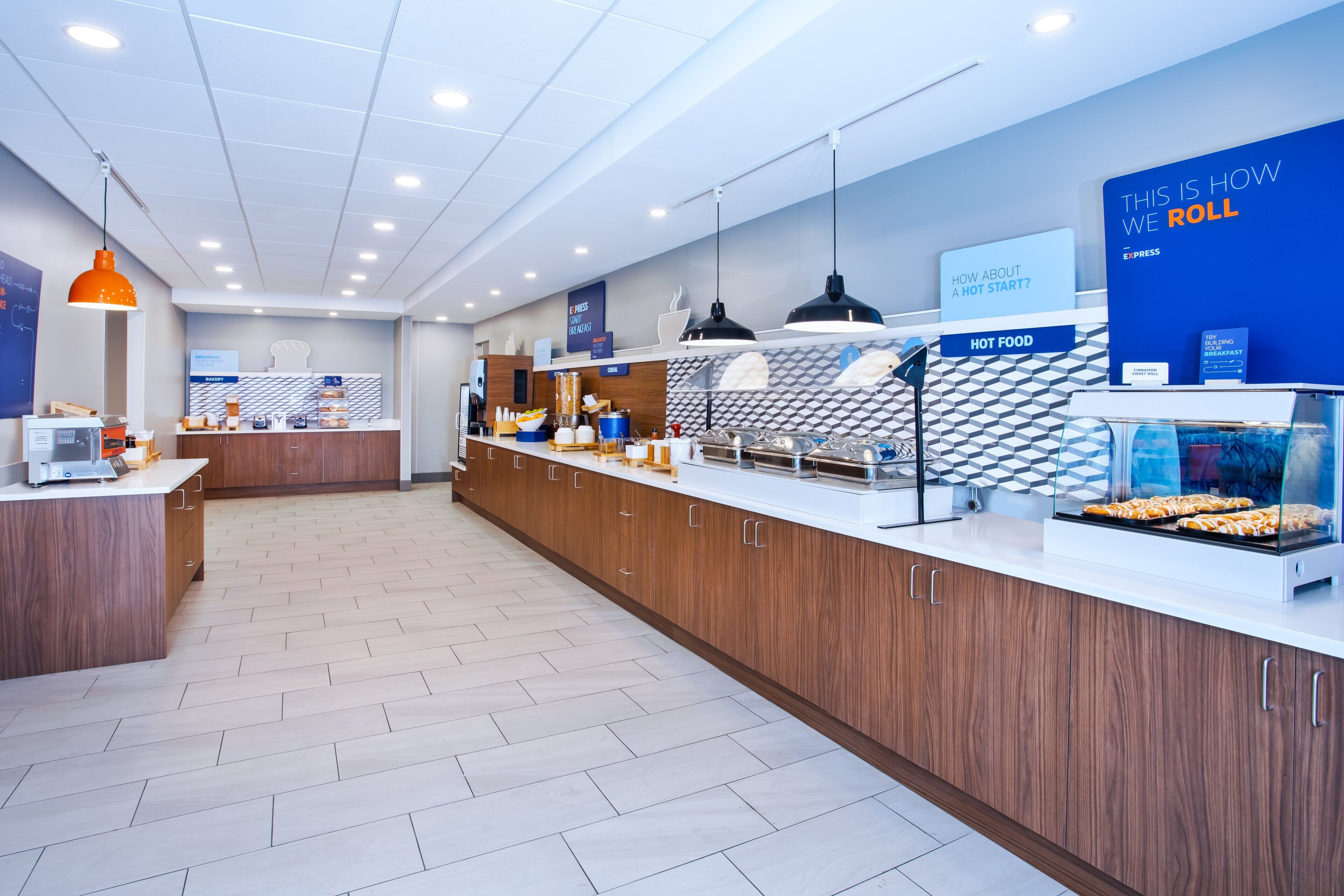 A modern breakfast area with wooden cabinets, a white countertop, and a display case with pastries.