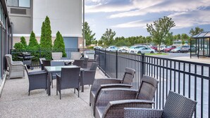 An outdoor patio with wicker furniture and a grill, overlooking a parking lot and trees.