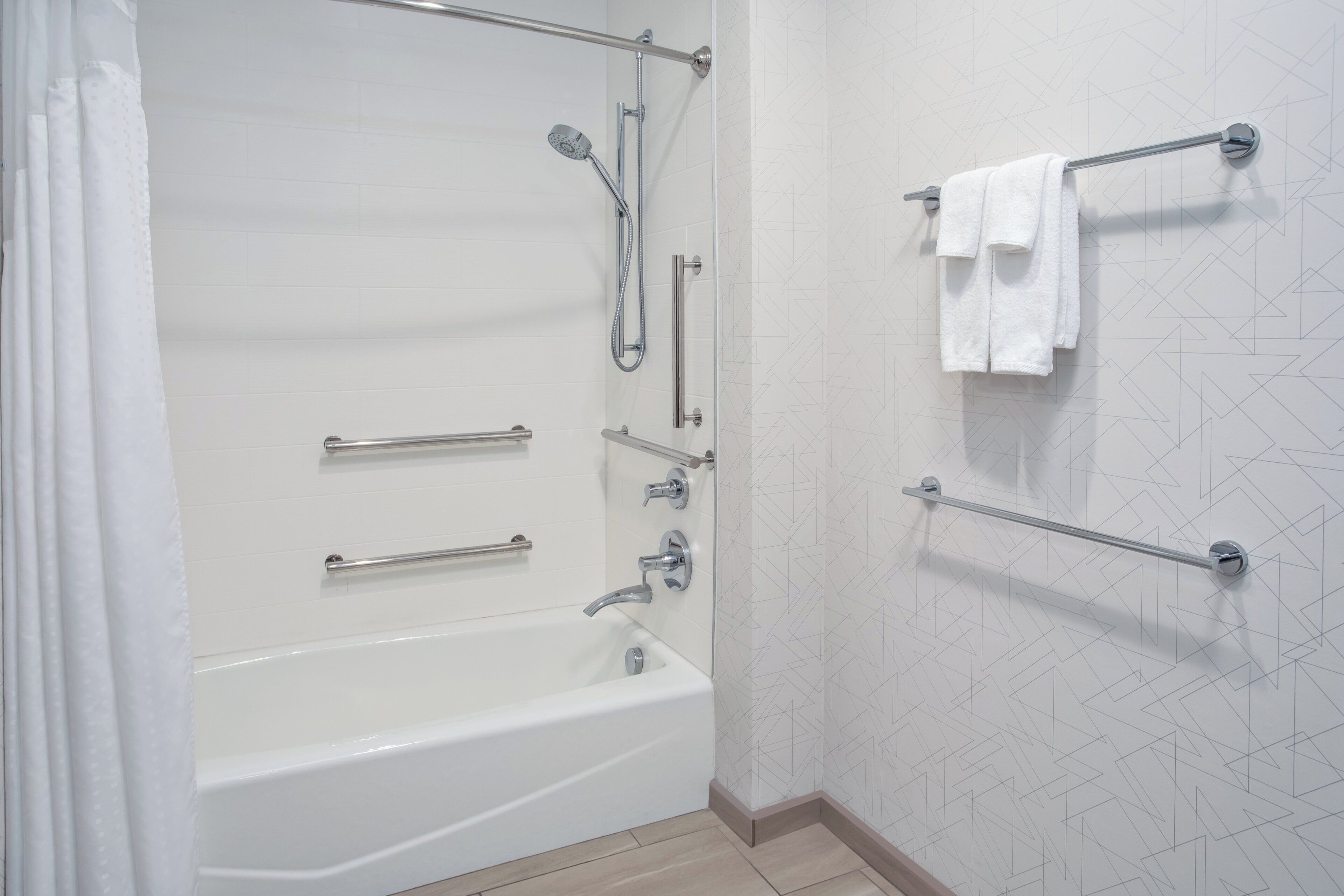 A modern bathroom with a bathtub, shower, and handrails.