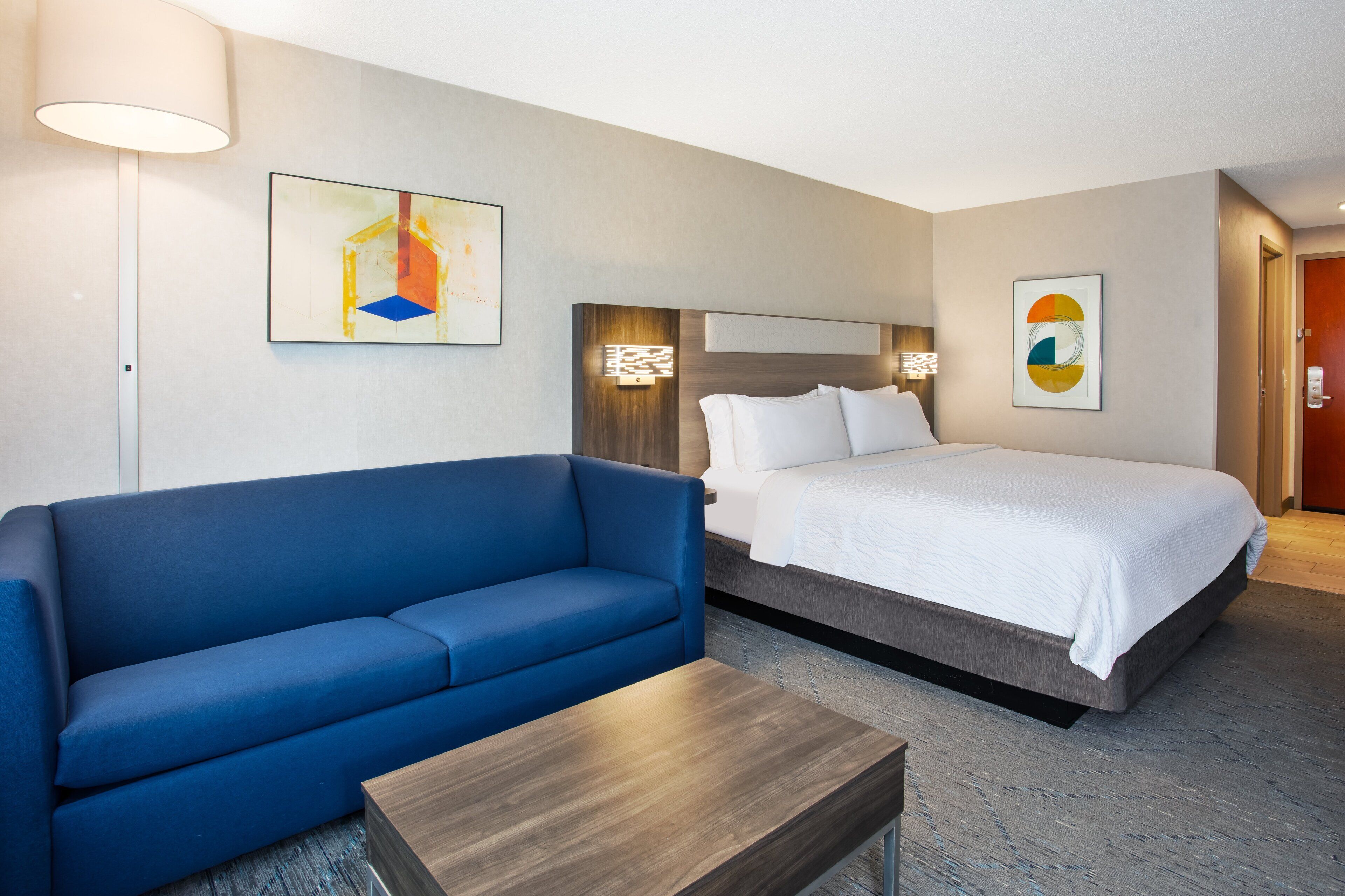 A hotel room with a bed, a blue sofa, a small table, and two wall-mounted lamps.