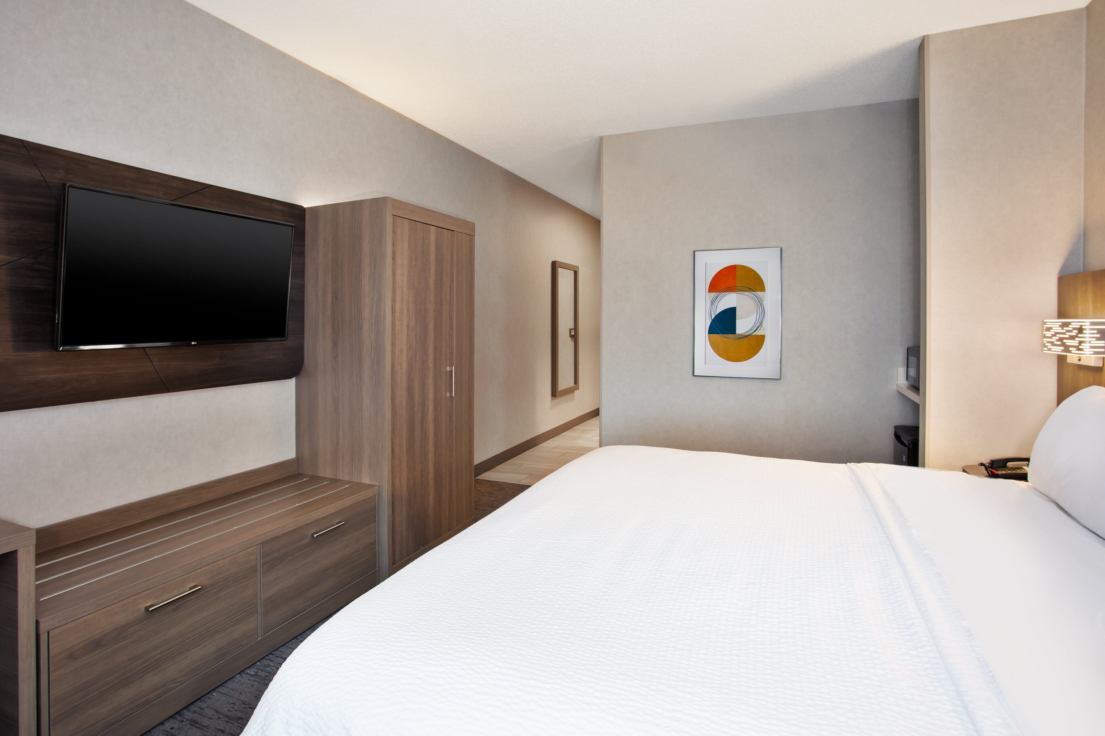 Et moderne hotelværelse med en stor seng, et fladskærms-tv på væggen, et garderobeskab og et indrammet kunstværk.