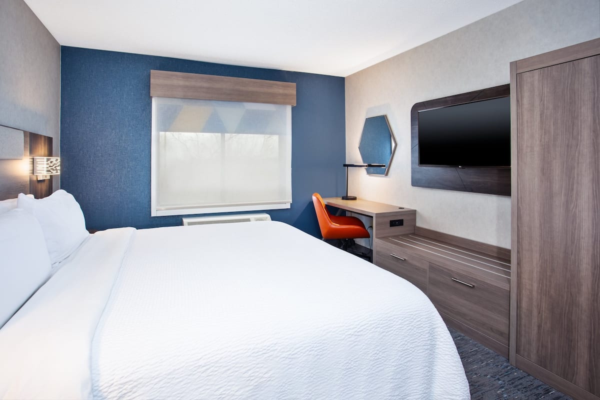 Habitación de hotel con una cama grande, un escritorio con silla, un televisor de pantalla plana en la pared y un armario.