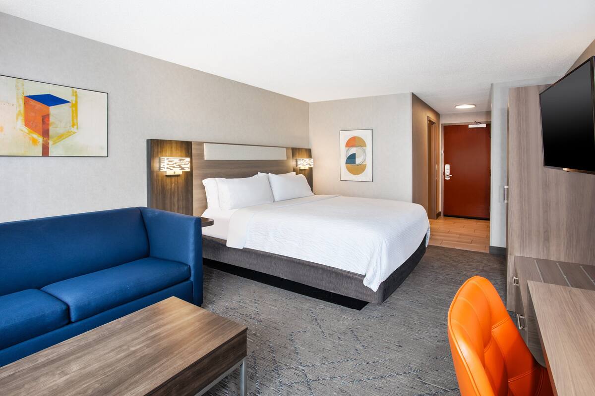 Una habitación de hotel moderna con una cama, un sofá azul, una mesa de madera y un televisor.