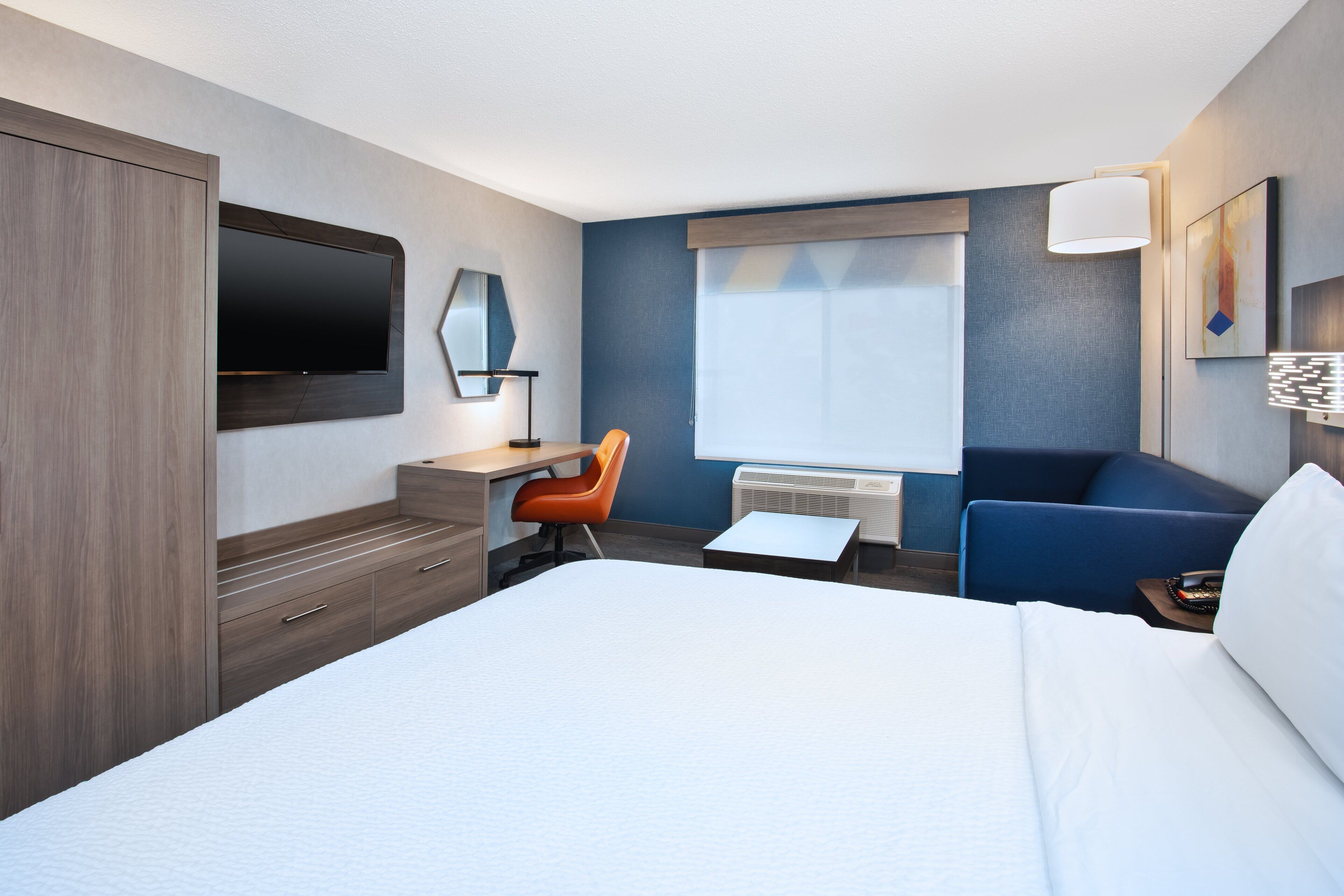 A hotel room with a bed, a desk, a chair, a TV, and a window.
