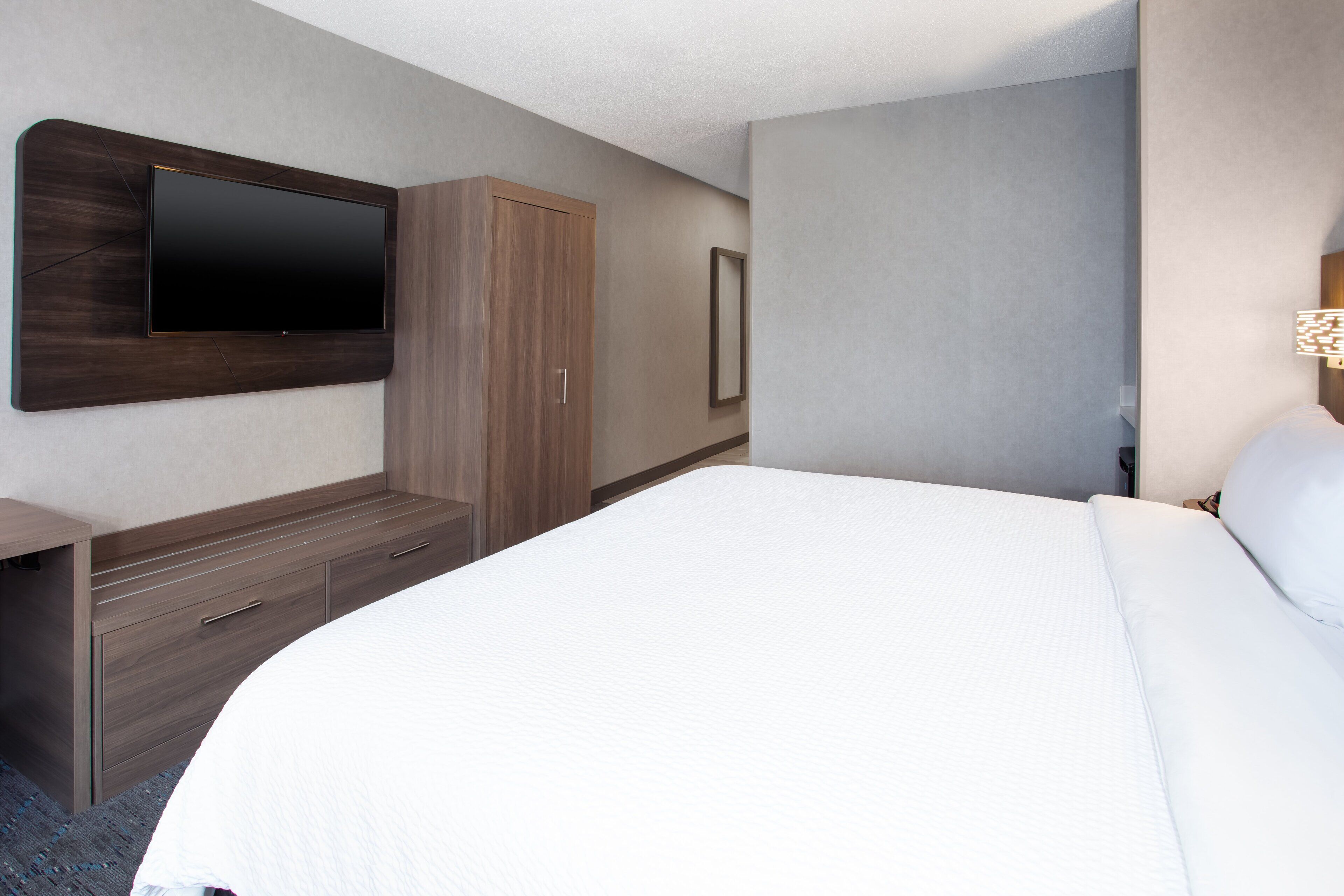 A hotel room with a large bed, a flat-screen TV mounted on the wall, a wardrobe, and a bedside table.