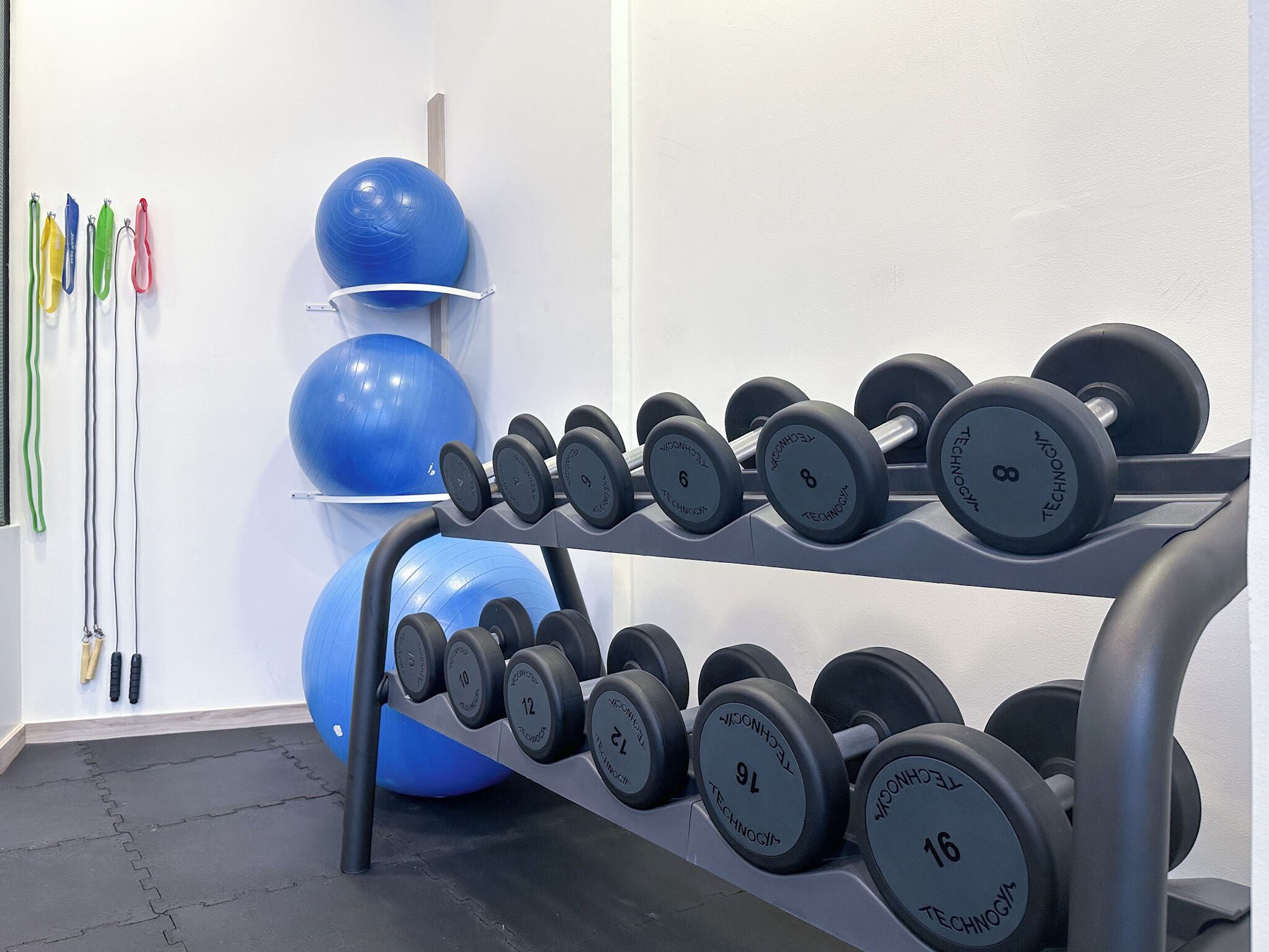 Un gimnasio con un estante de mancuernas y pelotas de ejercicio.