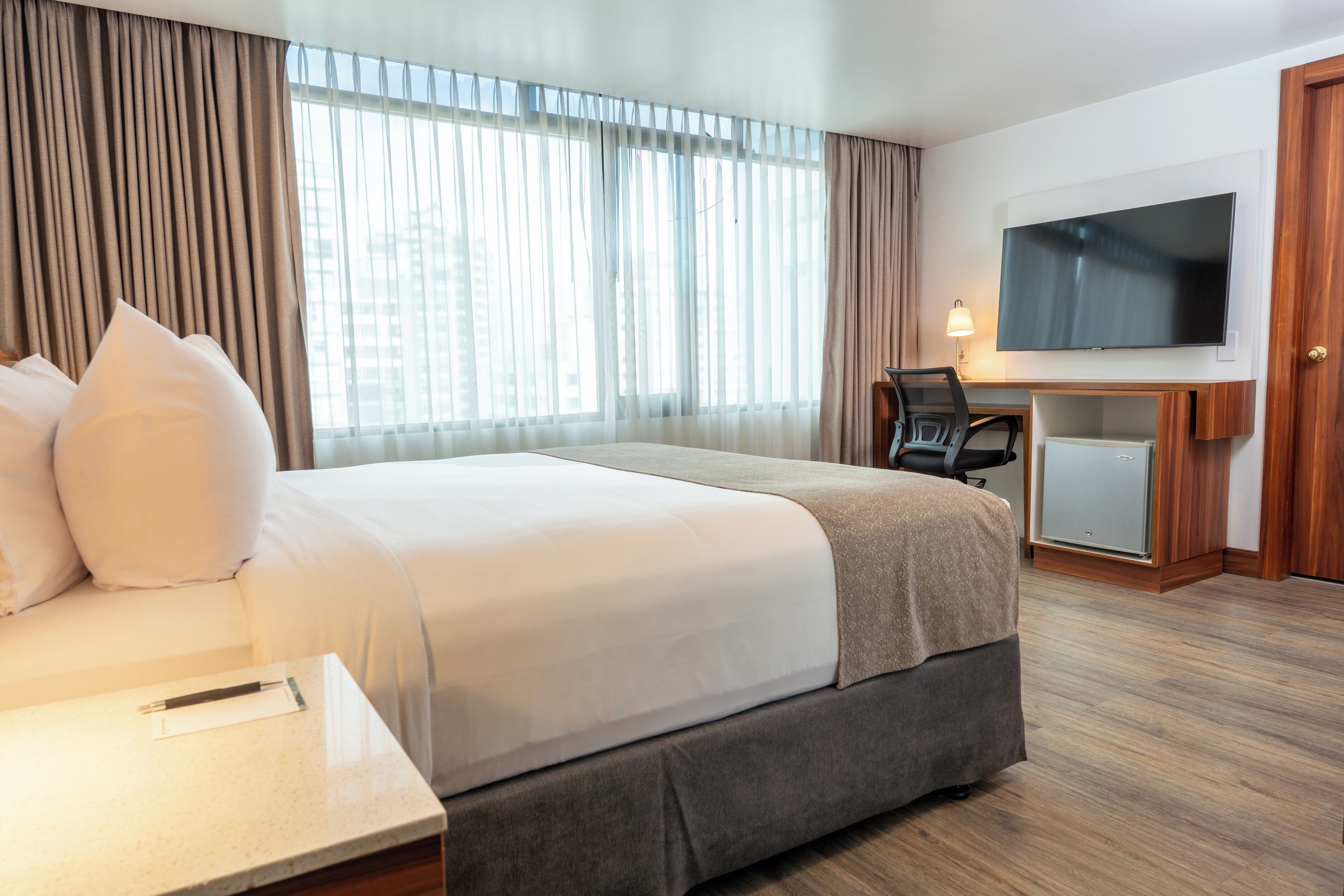 Une chambre d’hôtel avec un grand lit, un bureau avec une chaise, une télévision et une armoire.