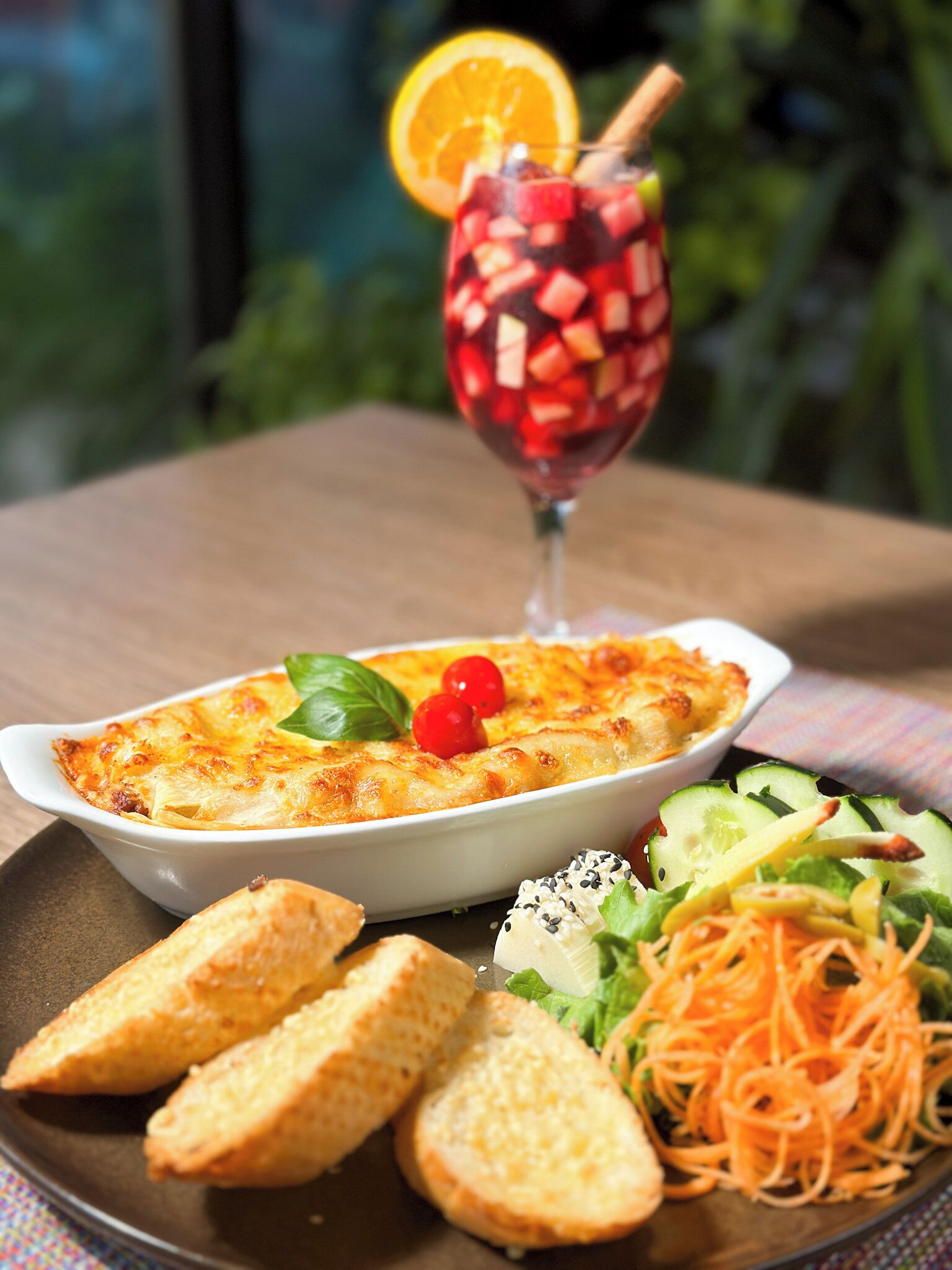 Una comida con un plato al horno, un vaso de bebida roja, pan y una ensalada.