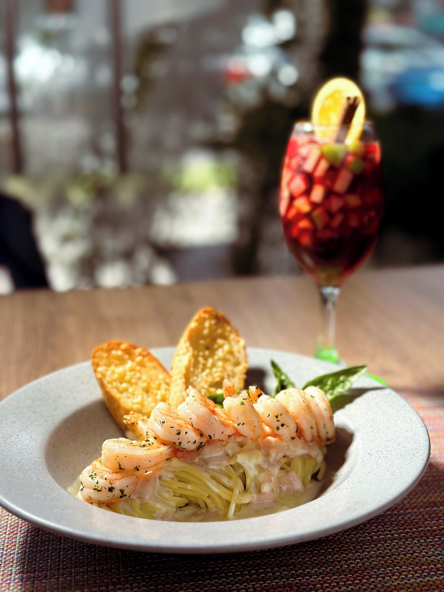 Un plato de camarones y pasta con un vaso de bebida roja con una rodaja de limón en el borde.