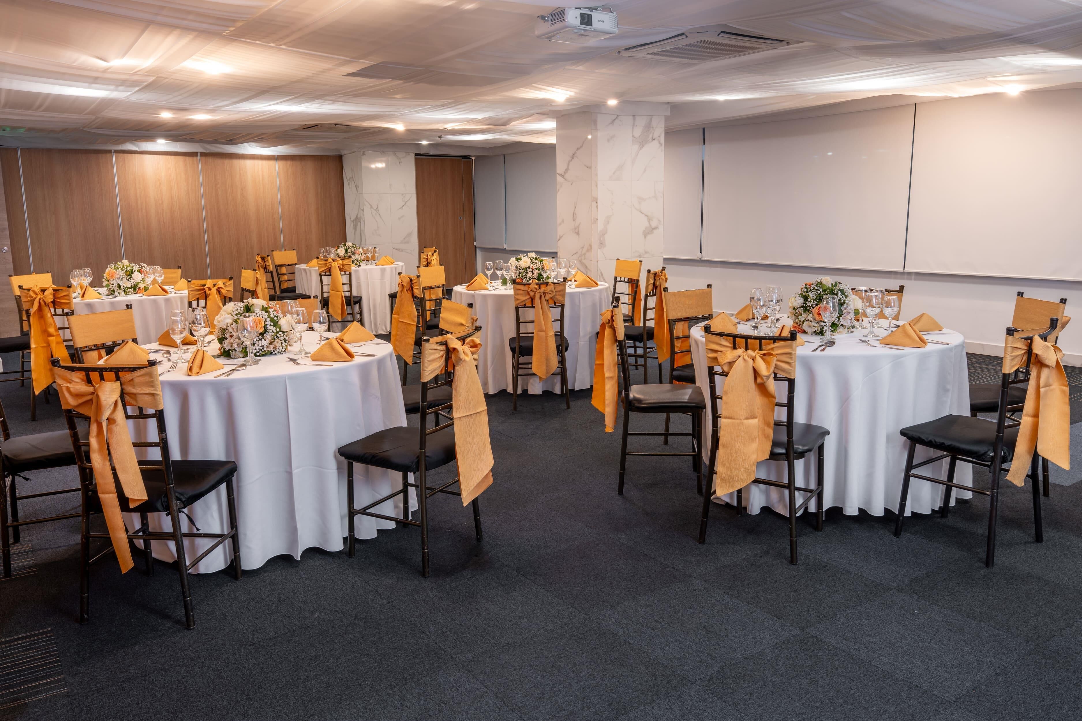 A conference room with round tables, each with a white tablecloth and orange chair covers.