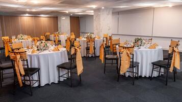 Une salle de conférence avec des tables rondes, chacune recouverte d’une nappe blanche et agrémentée de housses de chaise orange.