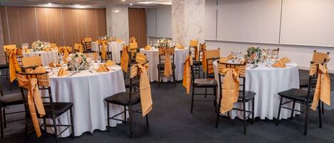 Un salón de conferencias con mesas redondas, cada una con mantel blanco y fundas naranjas para las sillas.