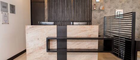 A reception desk with a marble top and black accents, flanked by vertical slats and a metal gate.