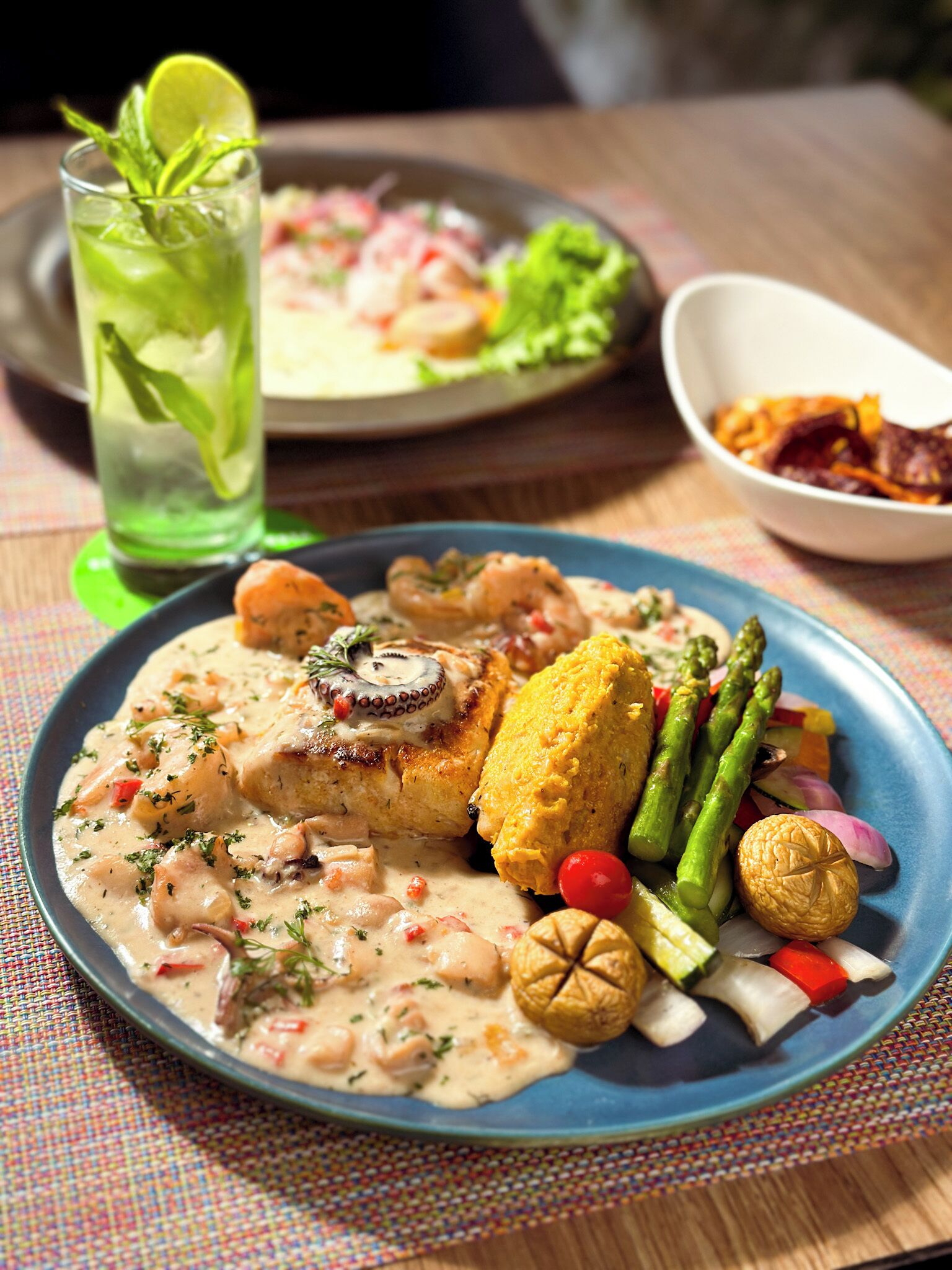 Prato de comida com frutos do mar, legumes e molho cremoso, servido em um prato azul.