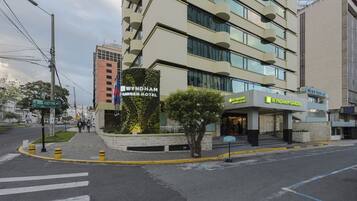 Et hotel med moderne design, der har en markant indgang og et anlagt område med et træ.