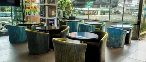 A modern cafe interior with round tables and chairs, a bar area with shelves of beverages, and a large window offering a view of the street.