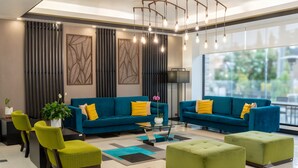 Una sala de estar moderna con dos sofás azules, sillas verdes, una mesa de centro de vidrio y un ventanal grande.