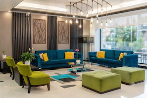 Una sala de estar moderna con dos sofás azules, sillas verdes, una mesa de centro de vidrio y un ventanal grande.