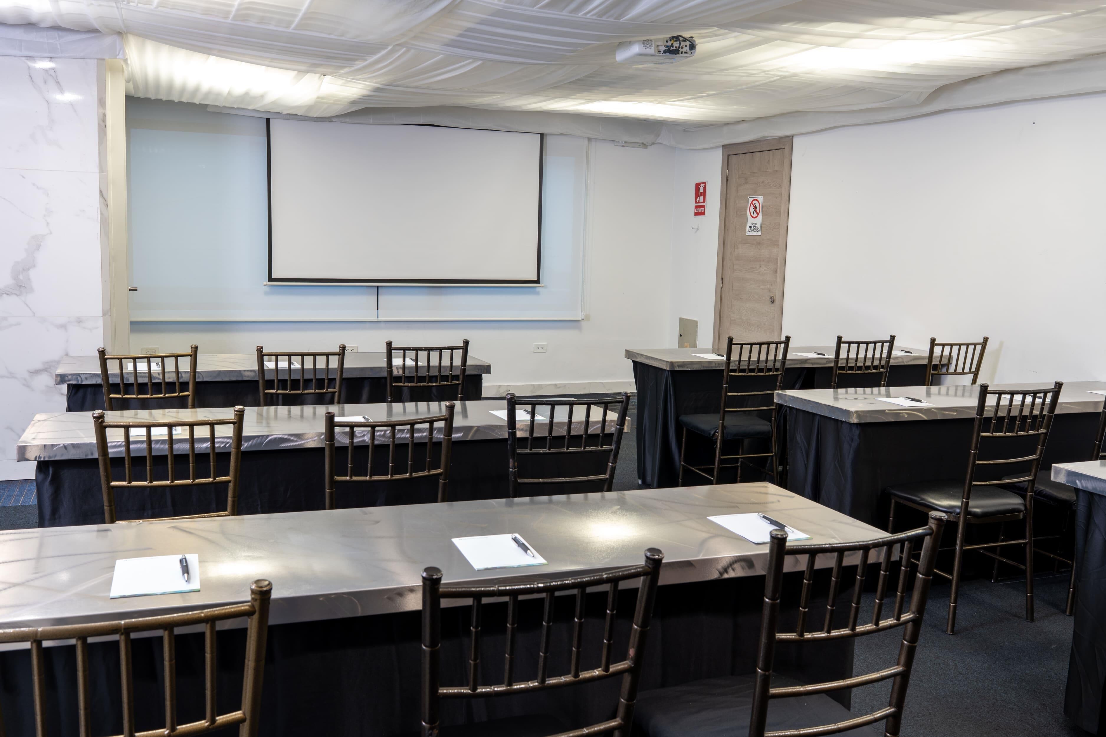 A conference room with multiple tables and chairs, a projector screen, and a whiteboard.