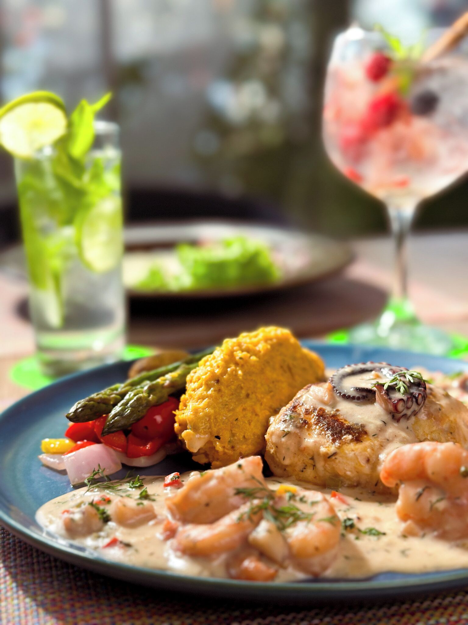 A plate of food with shrimp, chicken, and vegetables, and a glass of drink in the background.