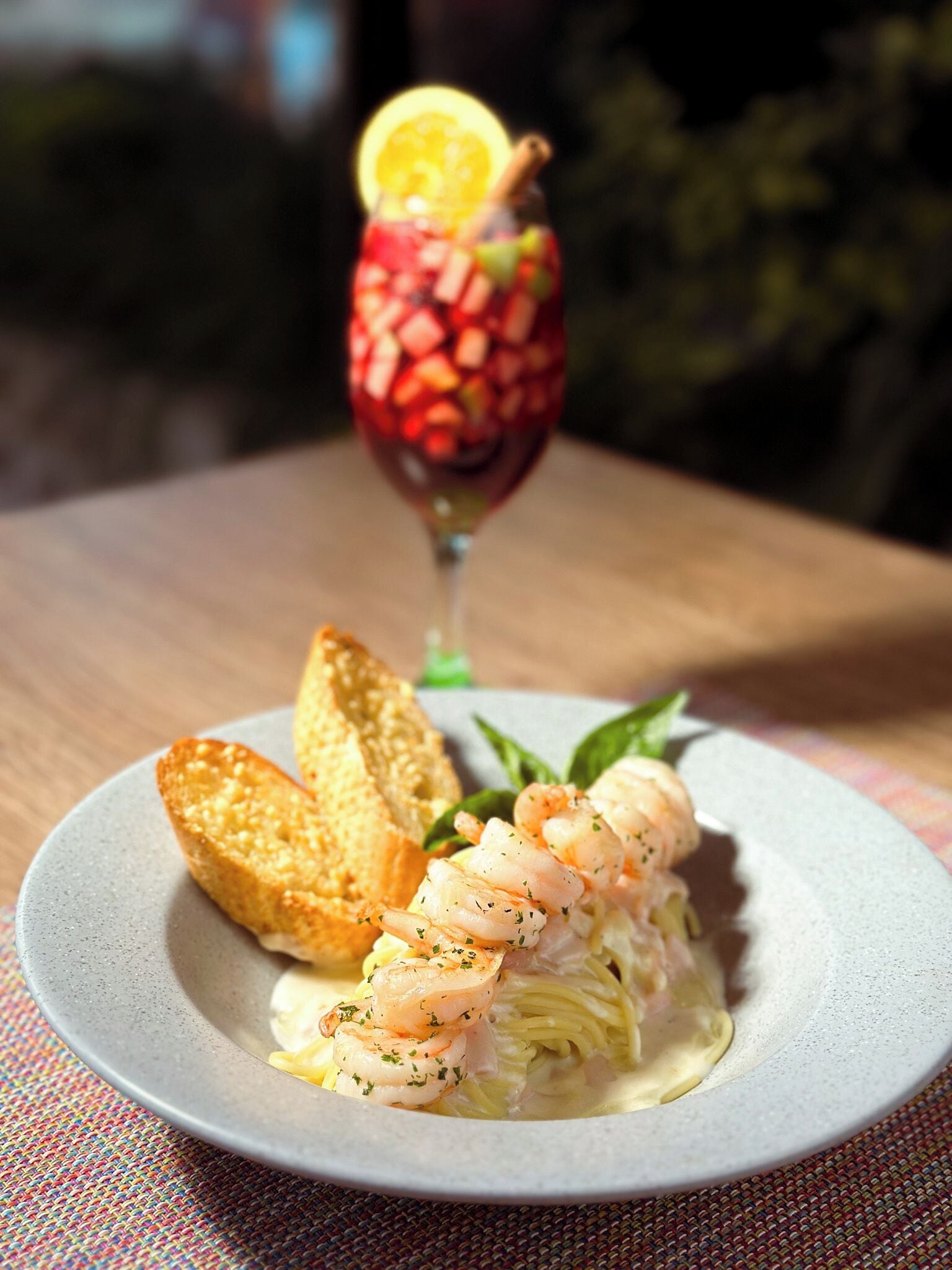 A plate of shrimp pasta with a glass of cocktail and toasted bread.