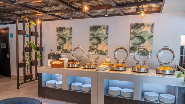 Zona de bufé con varias estaciones de comida, un área de estar con sillas y una pared decorada con arte abstracto.