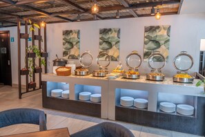 A buffet area with multiple food stations, a seating area with chairs, and a wall with abstract art. - Wyndham Garden Quito (Quito)