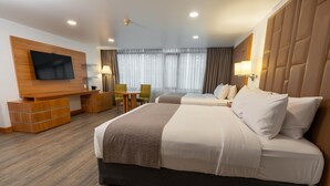 Habitación de hotel con una cama grande, televisor montado en la pared, escritorio con silla y ventana con cortinas.