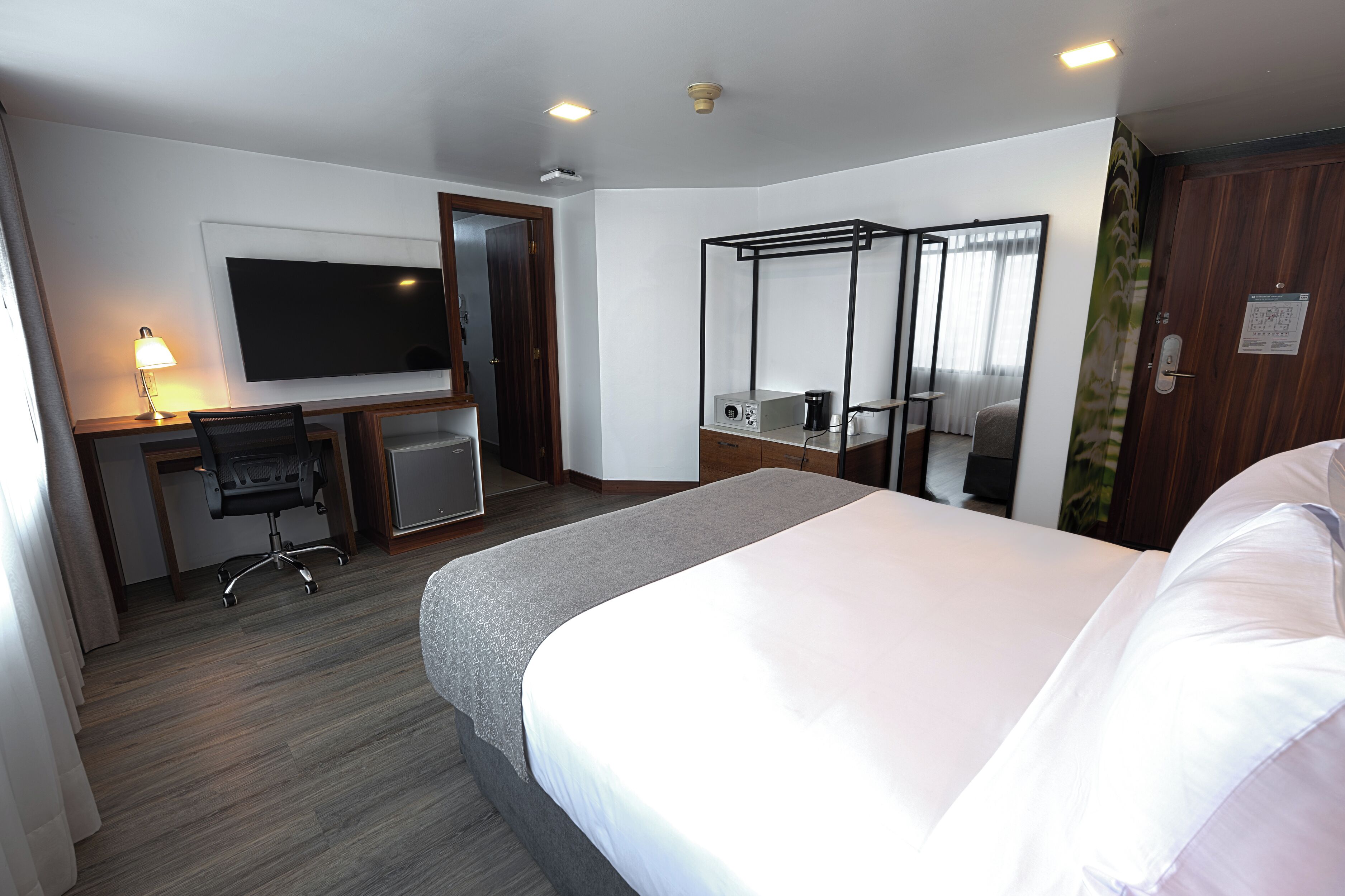 Una habitación de hotel con cama, escritorio, silla, televisión y un pequeño balcón.