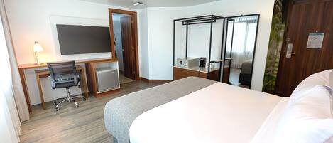 A hotel room with a bed, desk, chair, TV, and a small table with a lamp.