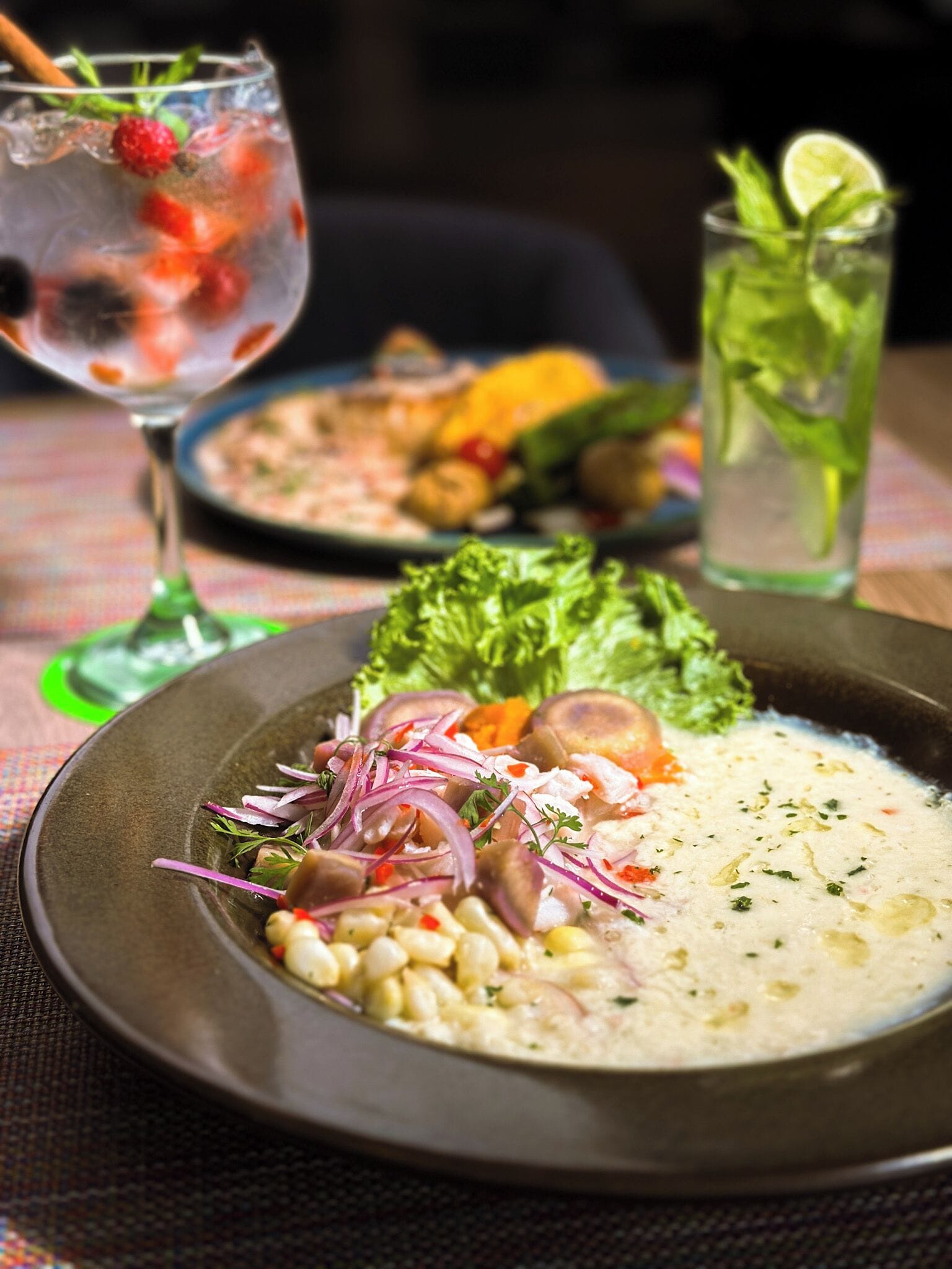 A plate of food with a creamy soup, corn, and red onions, accompanied by a glass of iced drink with berries and mint.