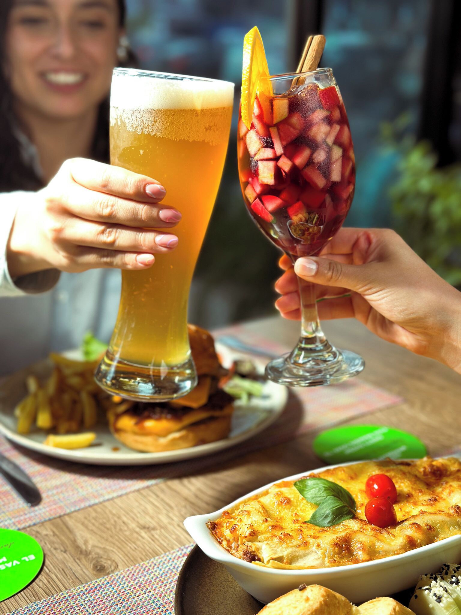 A person holding a tall glass of beer and a glass with fruit and a cinnamon stick.