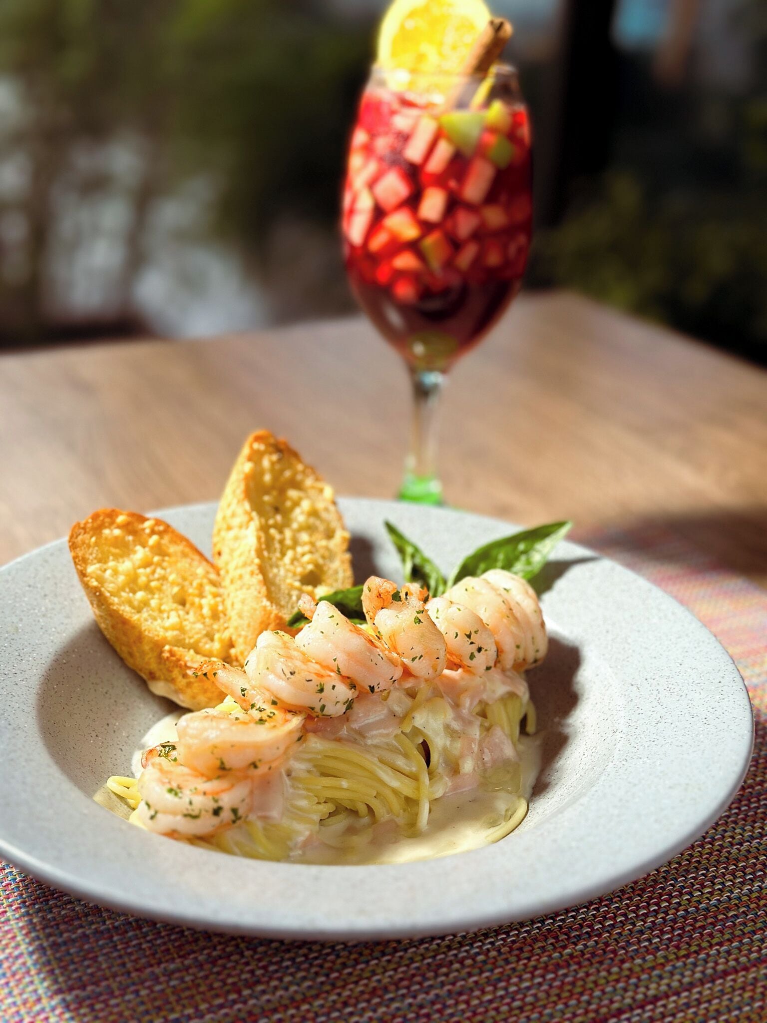 Un plato de pasta con camarones, un vaso de bebida roja y pan tostado sobre una mesa.
