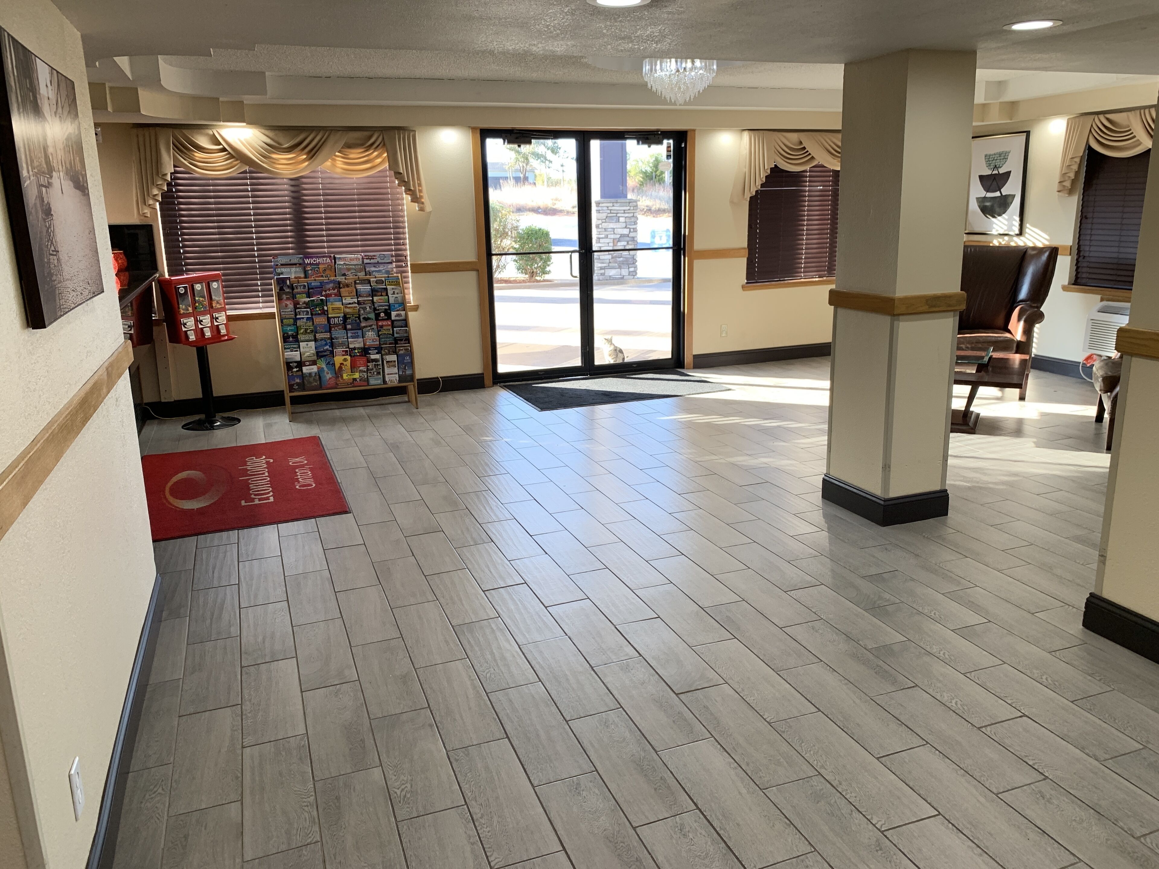 A hotel lobby with a reception desk, a magazine rack, and a red carpet leading to the entrance.