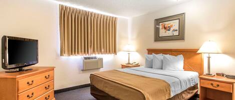 A hotel room with a bed, a TV, a dresser, a nightstand with lamps, an air conditioner, and a framed picture on the wall.