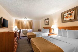 Quarto de hotel com duas camas, uma mesa, uma televisão e uma janela com cortinas.