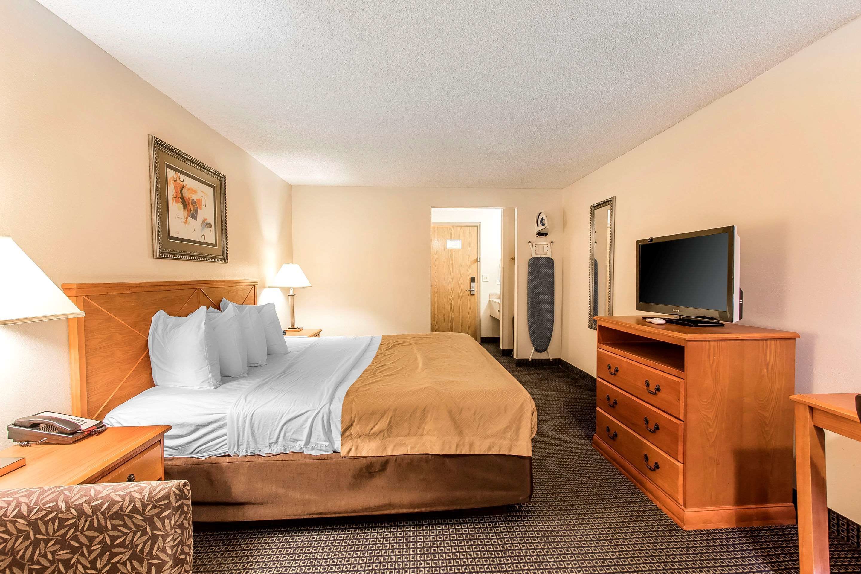 Une chambre d’hôtel avec un lit, un bureau, une télévision, une commode et une salle de bain visible à travers une porte ouverte.