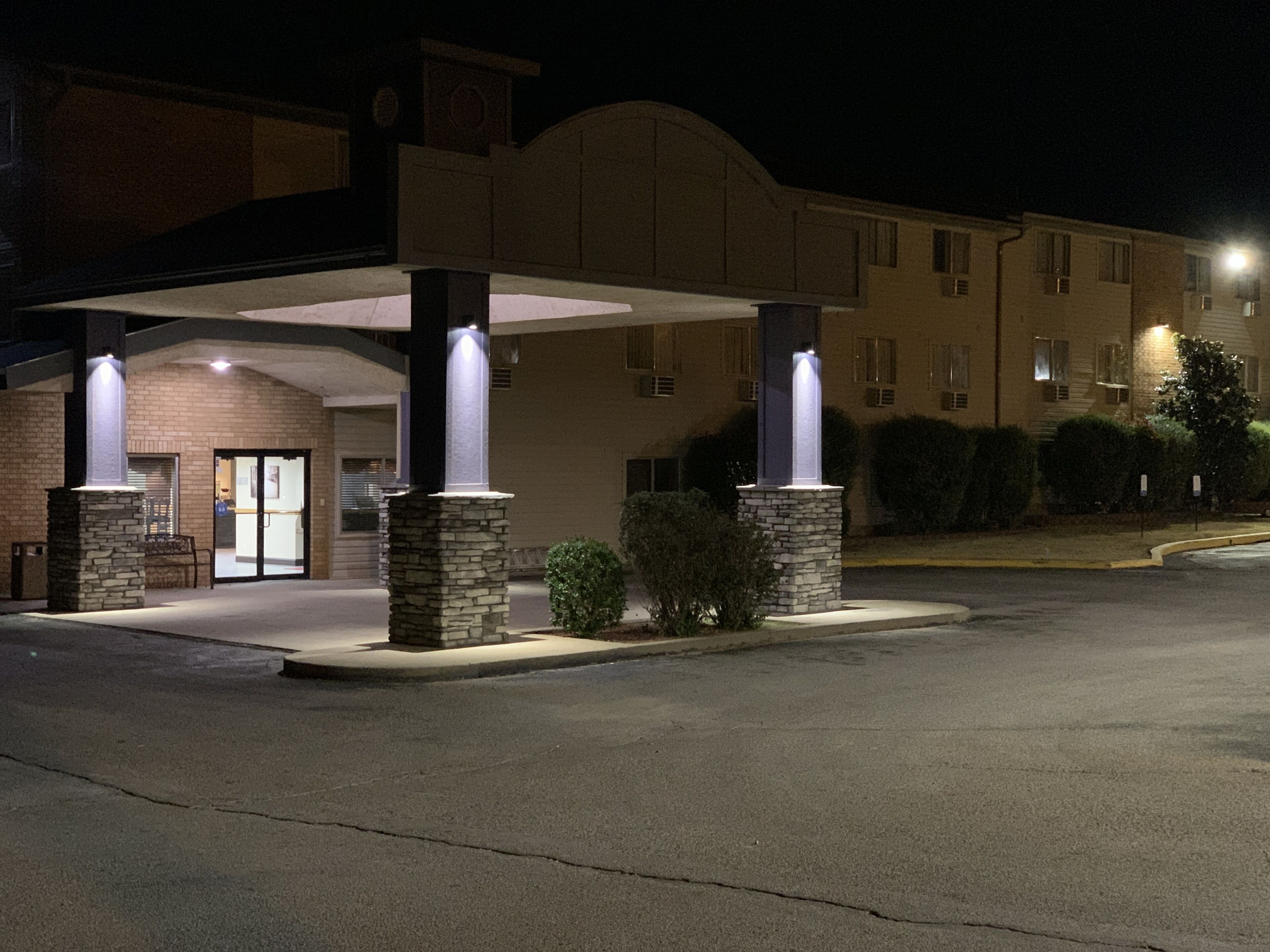 A hotel entrance with a covered walkway, stone pillars, and a well-lit facade.