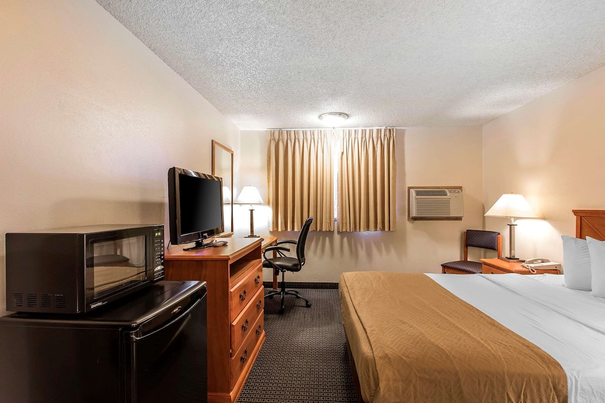 A hotel room with a bed, a desk with a computer, a television, a microwave, a lamp, and a window with curtains.
